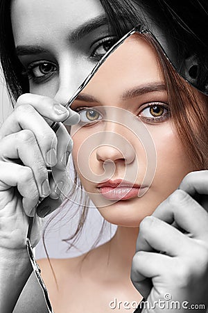 Monochrome portrait of female with mirror shard in hand posing on gray background. Color face reflection in mirror splinter Stock Photo