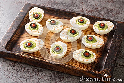 Monster eyes deviled eggs with a avocado and olives for Halloween day on a wooden tray. Horizontal Stock Photo