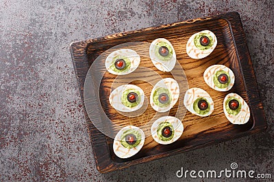 Monster eyes deviled eggs with a avocado and olives for Halloween day on a wooden tray. Horizontal top view Stock Photo
