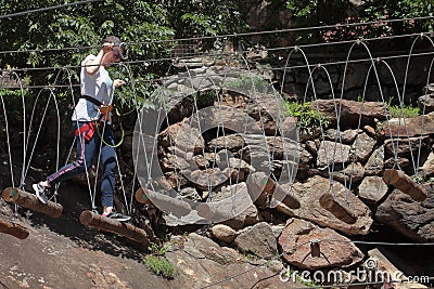 Montestrutto, Italian alps - June 2020: a girl walks along a Tibetan bridge rope-smeared cliff in an adventure park Editorial Stock Photo