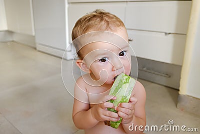 10-month-old baby sitting on the floor of her kitchen nibbling a slice of watermelon getting dirty all over Stock Photo