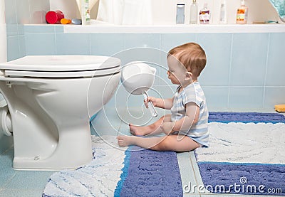 9 months old baby boy sitting in bathroom and looking on toilet Stock Photo