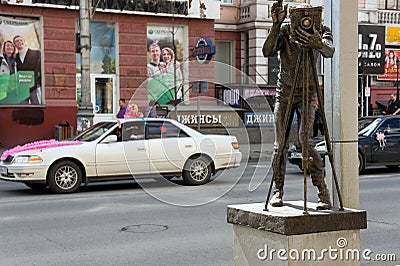 Monument to the photographer against the background of wedding cars on a city street. Editorial Stock Photo