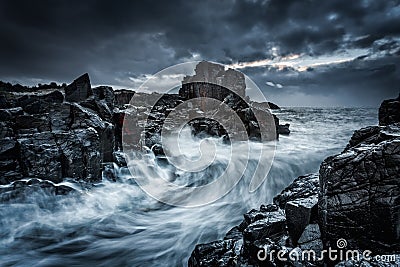 Moody dramatic skies and large waves crash onto coastal rocks Stock Photo