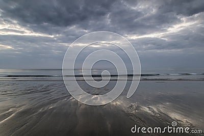 Moody ramatic sky reflected on wet beach landscape Stock Photo