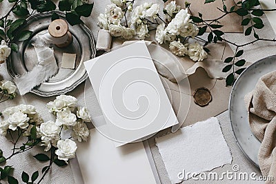 Moody wedding table mockup scene. Feminine desktop composition with fading white rose flowers, silver plate, silk Stock Photo