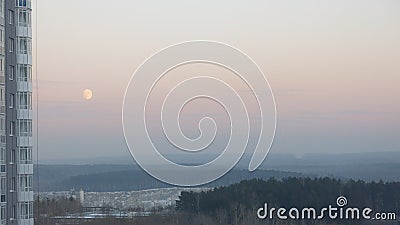 Moon in the evening sky over the forest next to a multi-storey building. Stock Photo
