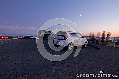 The moon glows above parked cars and people viewing the city of Victoria, BC, from the top of Mount Tolmie at sunset Editorial Stock Photo