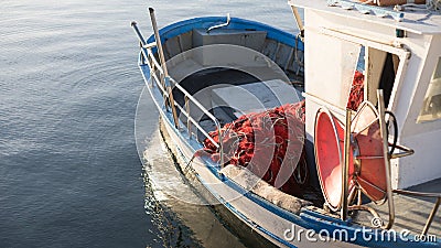 The moored fishing boat is lulled by the water while the sun reflects on the sea early in the morning with the winch of the Stock Photo