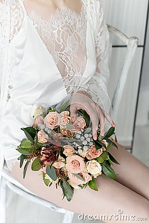 Morning beautiful delicate bride with short hair with a small wreath silk underwear sitting on a chair with a wedding bouquet Stock Photo