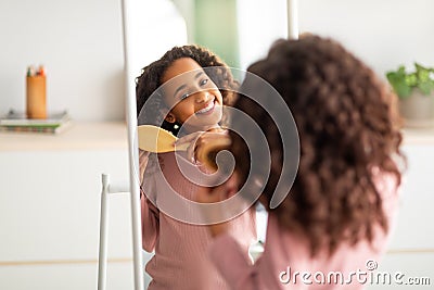 Morning beauty routine. Happy african american girl combing her curly hair with wooden comb, over shoulder view Stock Photo