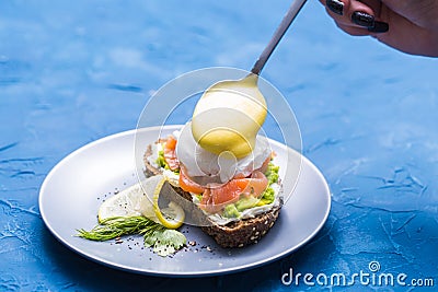 Morning and breakfast concept - Preparation of sandwich with salmon, spoon is pouring sauce on it. Stock Photo