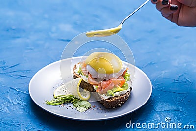 Morning and breakfast concept - Preparation of sandwich with salmon, spoon is pouring sauce on it. Stock Photo