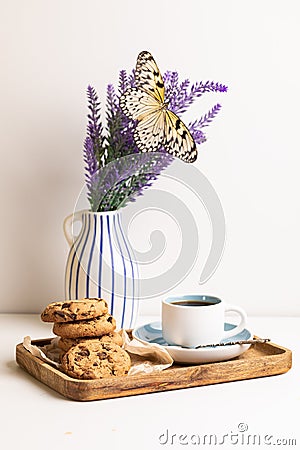 Morning breakfast, still life A wooden tray, a cup of coffee, chocolate cookies and a large butterfly on a bouquet Stock Photo