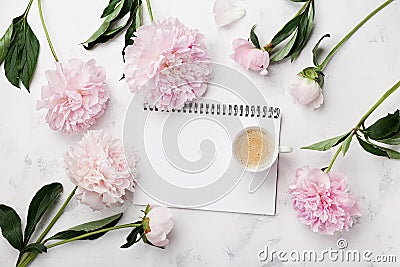 Morning coffee cup for breakfast, empty notebook and pink peony flowers on white stone table top view in flat lay style. Stock Photo