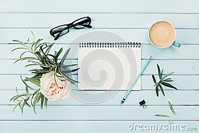 Morning coffee cup, clean notebook, pencil, eyeglasses and vintage rose flower in vase on blue rustic desk overhead view. Stock Photo