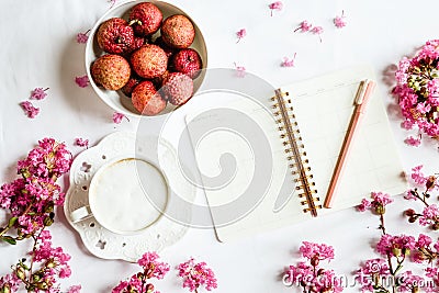 Morning coffee mug for breakfast, fresh lichee fruit, empty notebook, pen and pink flowers on white wooden table, top view, flat Stock Photo