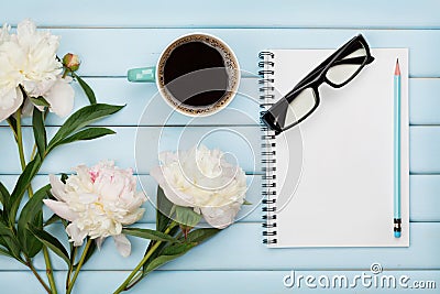 Morning coffee mug, empty notebook, pencil, glasses and white peony flowers on blue wooden table, cozy summer breakfast Stock Photo