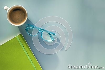 A morning coffee mug, a pair of blue reading glasses and a green notebook Stock Photo