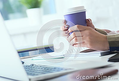 Morning coffee before a productive working day. Young female office worker holding coffee papercup and looking at the Stock Photo