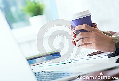 Morning coffee before a productive working day. Young female office worker holding coffee papercup and looking at the Stock Photo