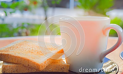 Morning coffee and toasted whole wheat bread on black plate on the red table with smoke over the cup of coffee in the sunshine. Stock Photo