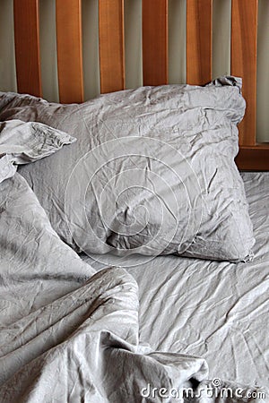 Morning empty messy bed gray bed linen, bedclothes. Sheet, blanket, pillows and wooden headboard Stock Photo