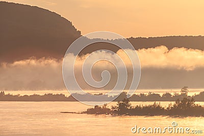 Morning fog rises over the river in the light of the rising sun against the silhouettes of mountains and Islands Stock Photo