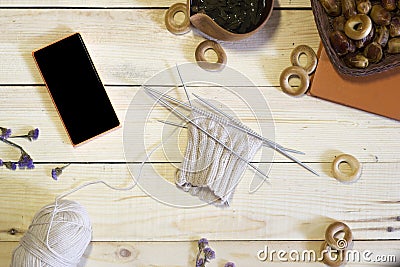 Morning for knitter, the composition of knitted product, phone, book, tea and dried fruits on wooden background Stock Photo