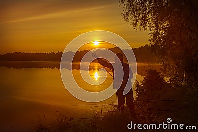 Morning on the lake dawn. A fisherman is standing on the shore next to fishing rods Stock Photo