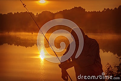 Morning on the lake dawn. A fisherman is standing on the shore next to fishing rods Stock Photo