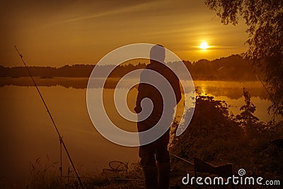 Morning on the lake dawn. A fisherman is standing on the shore next to fishing rods Stock Photo