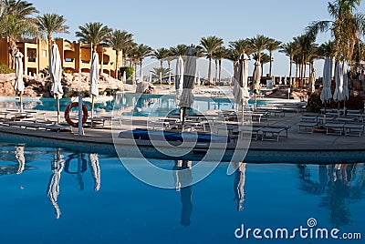 Morning pool side in hotel. No people near swimming pool. Closed pool umbrellas. Water pool reflex in the calm water. Palms on sea Editorial Stock Photo