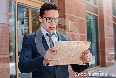 Morning routine. Businessman in eyeglasses standing on the city street looking at newspaper shocked close-up Stock Photo