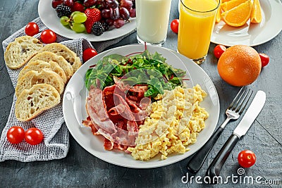 Morning Scrambled egg, bacon breakfast with orange juice, milk, fruit, bread on white plate Stock Photo