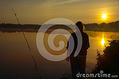 Morning on the lake dawn. A fisherman is standing on the shore next to fishing rods Stock Photo