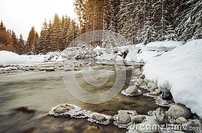 Morning sun shines on forest river creek in winter, rocks on shore covered with snow, long exposure makes water silky smooth Stock Photo