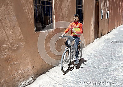 Moroccan schoolboy riding his bicycle home along a narrow street in the medina quarter near Jemaa el-Fnaa Square. Editorial Stock Photo