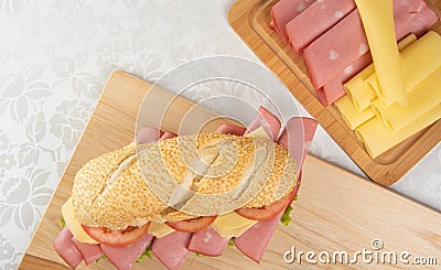 Mortadella sandwich, lettuce, tomato and cheese on a polished board and slices of mortadella and cheese next to it on a cold board Stock Photo