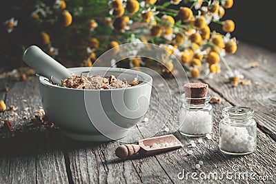 Mortar of dried healing herbs, homeopathic globules and bunch of chamomile plant. Stock Photo