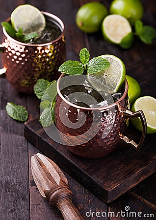 Moscow mule cocktail in a copper mug with lime and mint and wooden squeezer on dark wooden background Stock Photo