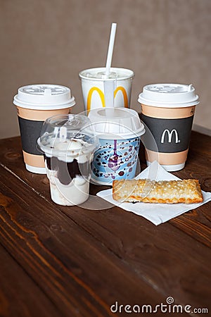 Moscow, Russia - April 06, 2019: McDonald`s food delivery. Desserts and hot drinks on wooden table. Close-up. Side view. Vertical Editorial Stock Photo