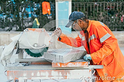 Moscow, Russia - August 14, 2015: a builder cuts a piece of granite stone on a circular saw machine. Reconstruction of Editorial Stock Photo