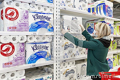 Moscow, Russia, 03/26/2020: A blond woman in a medical mask buys a lot of toilet paper in a supermarket. Panic and deficiency Editorial Stock Photo