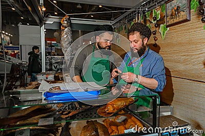 Moscow, Russia - February 25, 2017: Two bearded seller of dried and smoked fish at the time of the break at work on fair Editorial Stock Photo