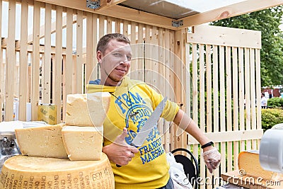 A cheese seller in a yellow sweater offers cheese to a customer Editorial Stock Photo