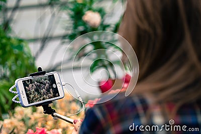 MOSCOW, RUSSIA - MARCH 12, 2018: A visitor makes photos of flowers on the phone on a self-stick in the Aptekarsky Ogorod. Editorial Stock Photo