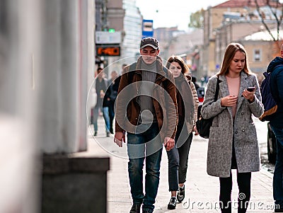 Group of people walks in a crowd of people dressed in demi-season clothes along the street. Warm autumn sunny day. City life. Side Editorial Stock Photo