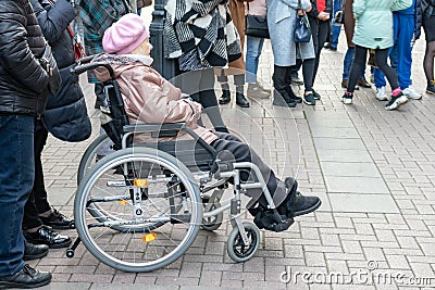 Moscow, Russia - October 19, 2019: A senior disabled woman in a wheelchair watching and listening street musicians Editorial Stock Photo