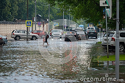 Woman crossing street flooded with water after heavy rain, cars driving through flood Editorial Stock Photo